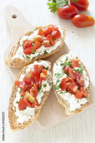 Crostini with cottage cheese, parsley and tomato on cutting boar