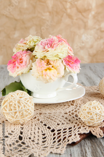 Roses in cup on napkins on  wooden table on beige background