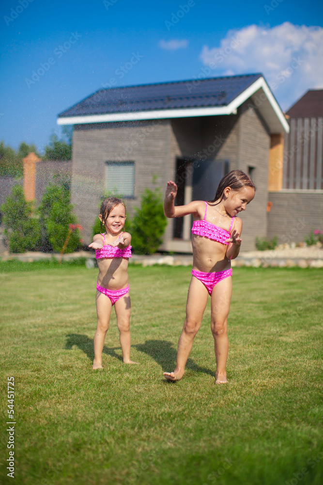 Fototapeta premium Two little sisters frolicing and splashing in their yard