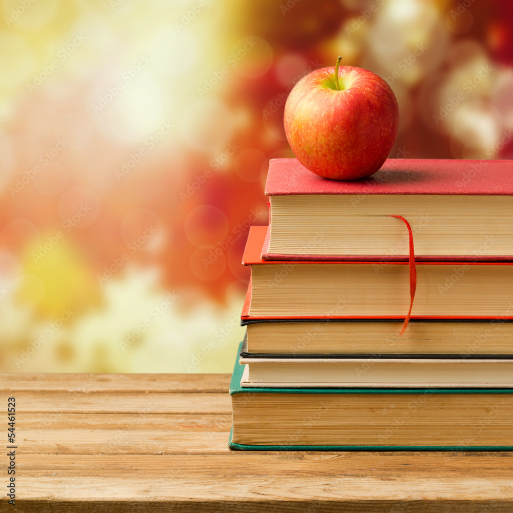 Naklejka premium Old vintage books and apple over autumn leaves bokeh background