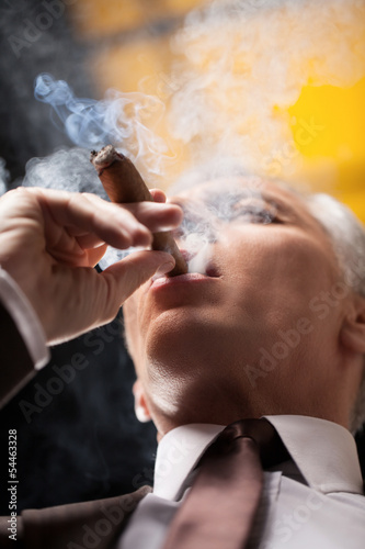 Smoking a good cigar. Low angle view of senior businessman smoki