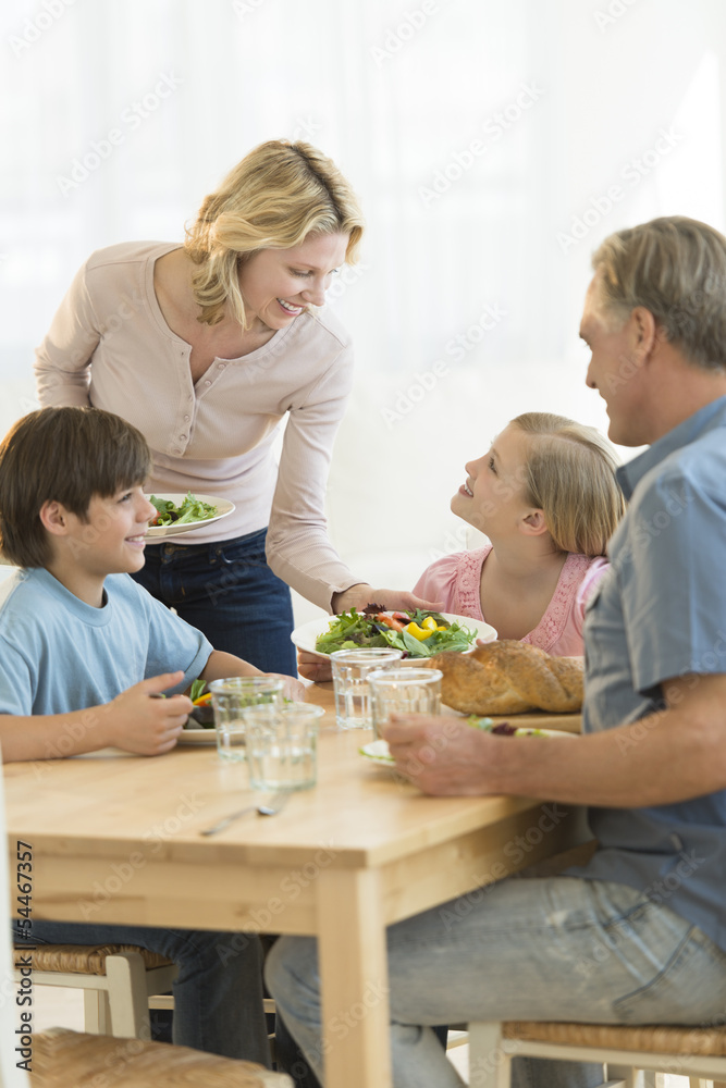 Woman Serving Food To Daughter At Dining Table Woman Serving Food To Daughter At Dining Table