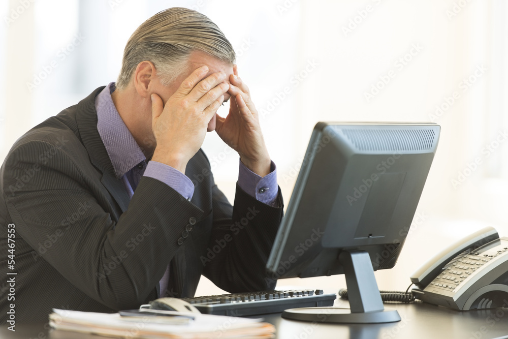 Businessman With Head In Hands Sitting At Desk Businessman With Head In Hands Sitting At Desk