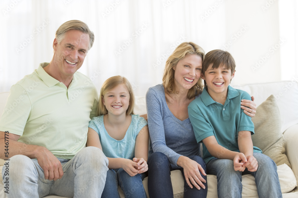 Family Of Four Smiling Together On Sofa