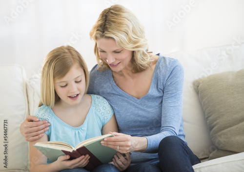 Mother And Daughter Reading Book Together On Sofa