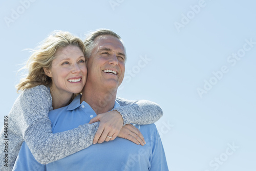 Woman Embracing Man From Behind While Looking Away Against Sky