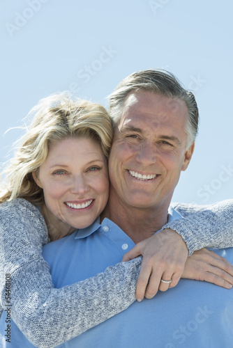 Beautiful Woman Embracing Man From Behind Against Clear Sky