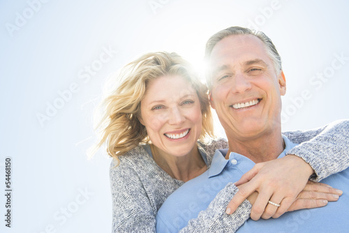 Cheerful Woman Embracing Man From Behind Against Sky