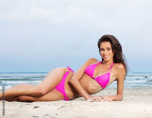A young brunette woman in pink bikini relaxing on the beach © Acronym