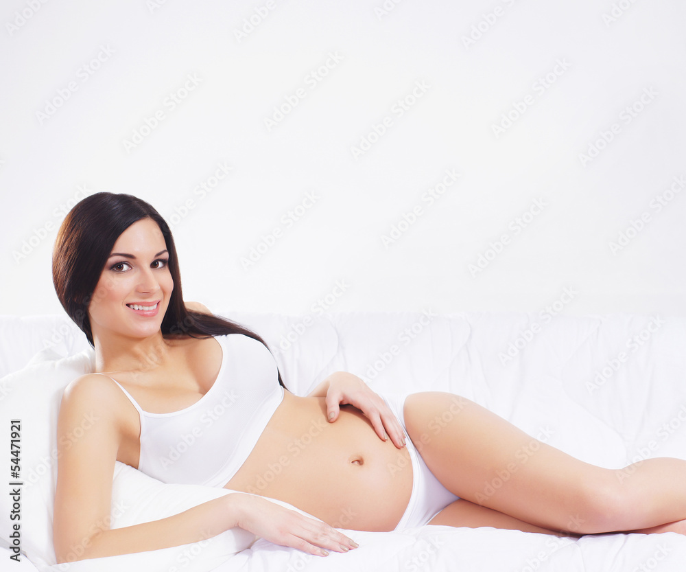 A young pregnant brunette woman laying in white lingerie A young pregnant brunette woman laying in white lingerie