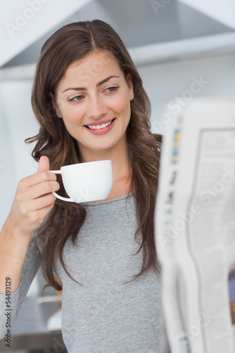 Woman reading a newspaper while holding a cup of coffee