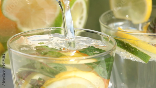 Jug with fresh lemonade pouring to glass