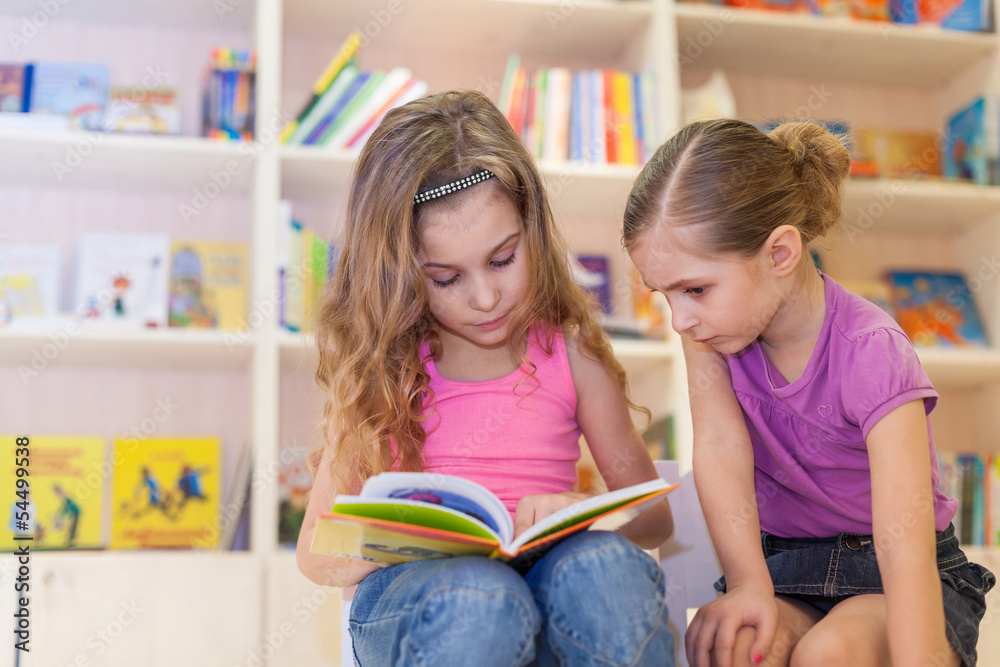 Two girls are reading an interesting book in library Two girls are reading an interesting book in library