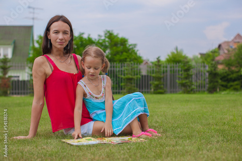 young mother and her cute daughter reading a book and enjoying
