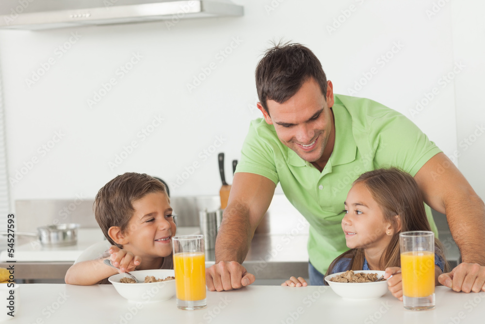 Father chatting to his children while they are having breakfast Father chatting to his children while they are having breakfast