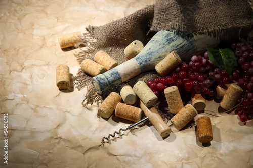 Old bottle of wine, grapes and corks on old paper background