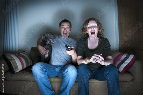 middle aged couple and dog laughing at the television photo