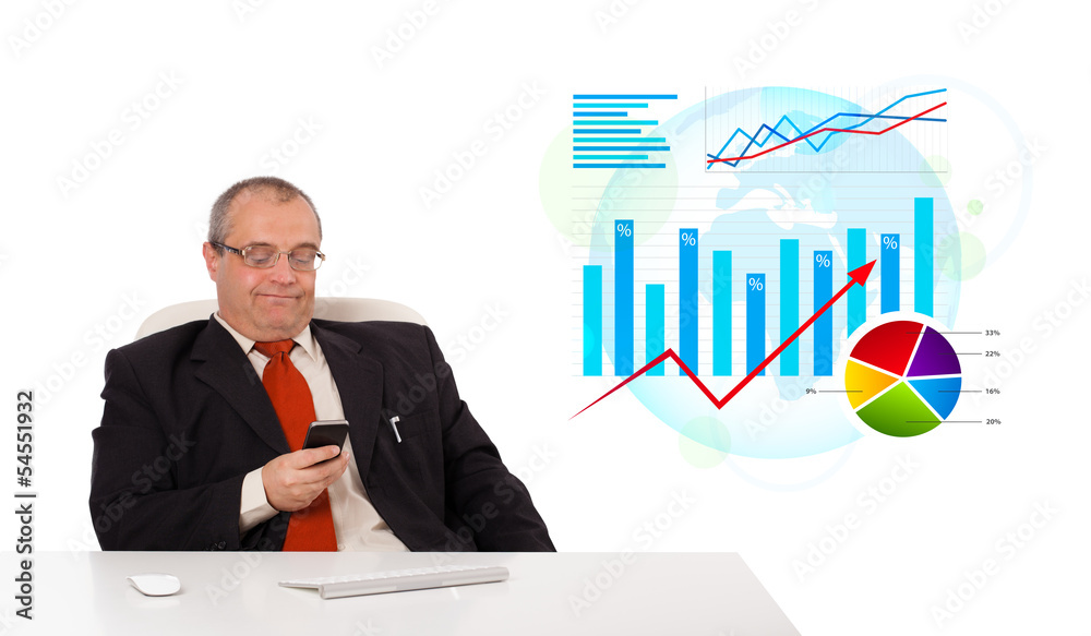 Businessman sitting at desk with statistics and holding a mobile Businessman sitting at desk with statistics and holding a mobile