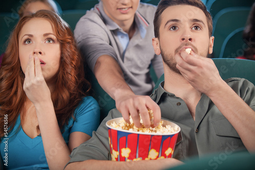 Принти на полотні Stealing popcorn. Young men stealing popcorn during the movie se