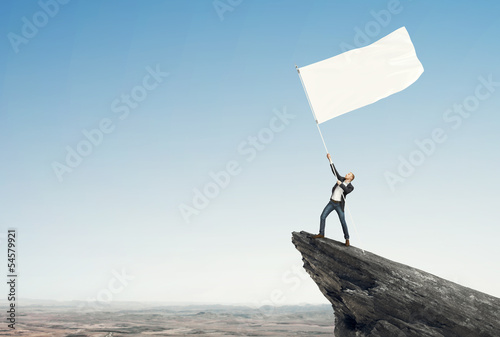 Quadro su tela man with blank flag standing on the top of a rock