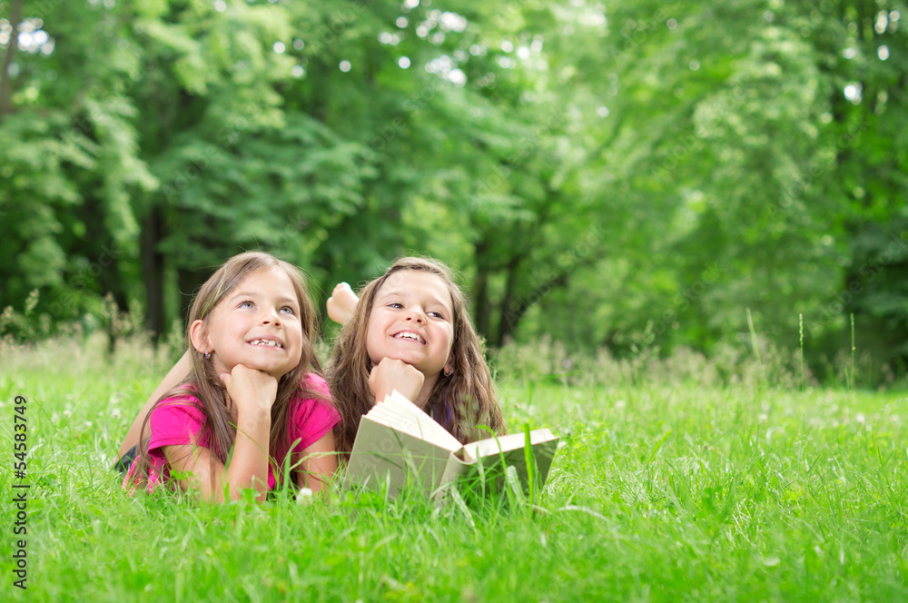 Two happy Girls lying with Book in the Park