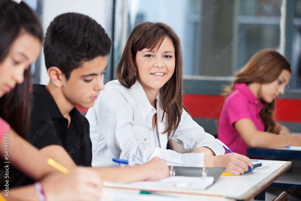 Girl With Classmates Sitting At Desk In Classroom Girl With Classmates Sitting At Desk In Classroom