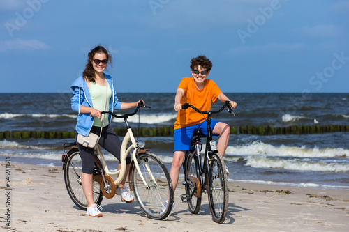 Healthy lifestyle - teenage girl and boy biking on beach