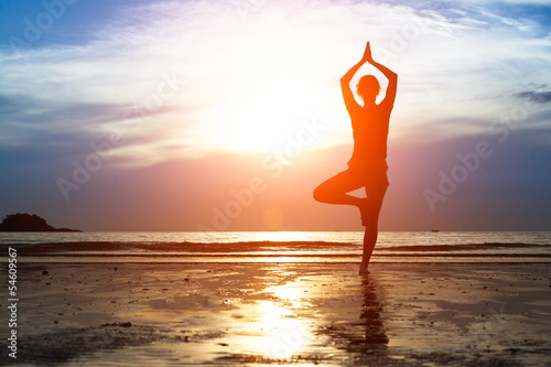 Silhouette woman practicing yoga on the beach at sunset.