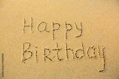 Inscription Happy Birthday on texture of wet sand.