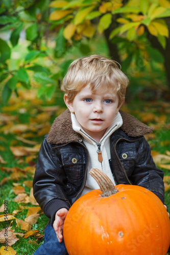 Little toddler with big orange pumpkin in garden