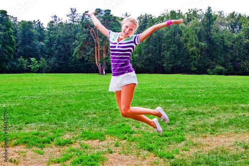 young and beautiful woman jumping on a summer lawn