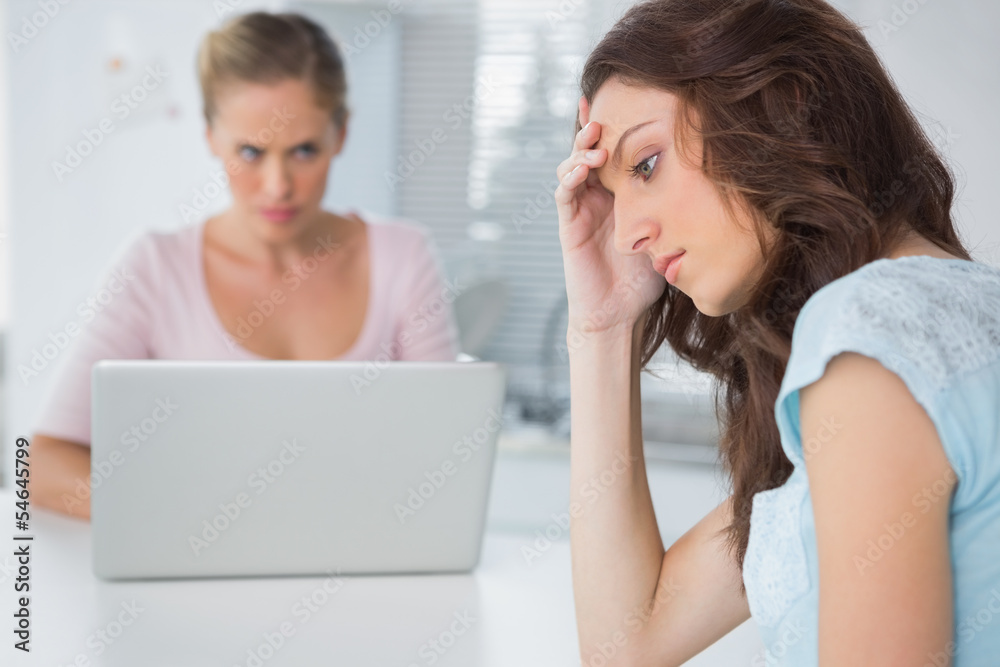 Upset woman thinking while her angry friend is staring at her Upset woman thinking while her angry friend is staring at her