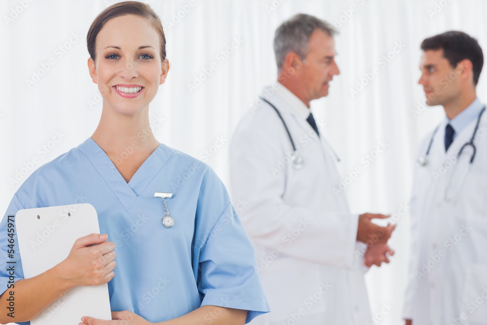 Smiling surgeon posing while doctors talking on background Smiling surgeon posing while doctors talking on background