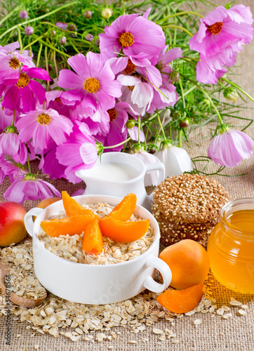 Oatmeal with apricot, milk jug, cookies, honey and flowers