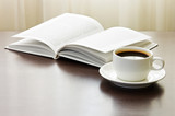 Cup of coffee and opened book on table against window