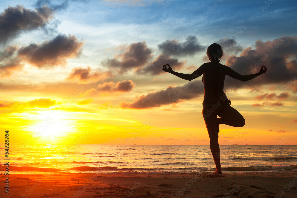 Young woman practicing yoga on the beach during the sunset.