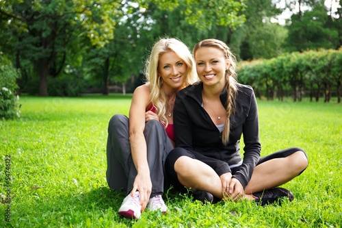 Two smiling athletic girls sitting on a grass in a park