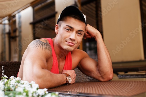 Stylish young man in cap sitting behind table 