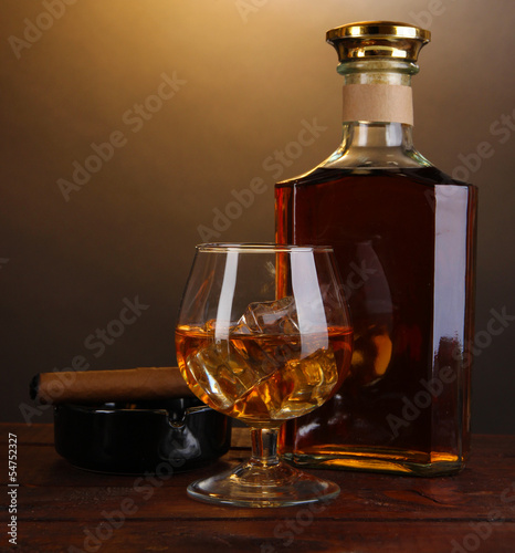 Brandy with ice on wooden table on brown background