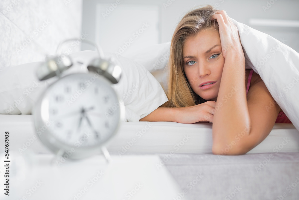Exhausted blonde looking at camera with alarm clock in foregroun