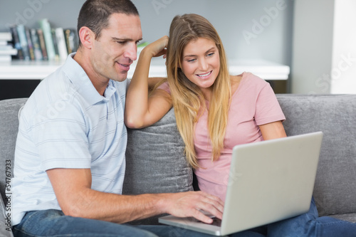 Happy couple sitting using laptop on the couch together