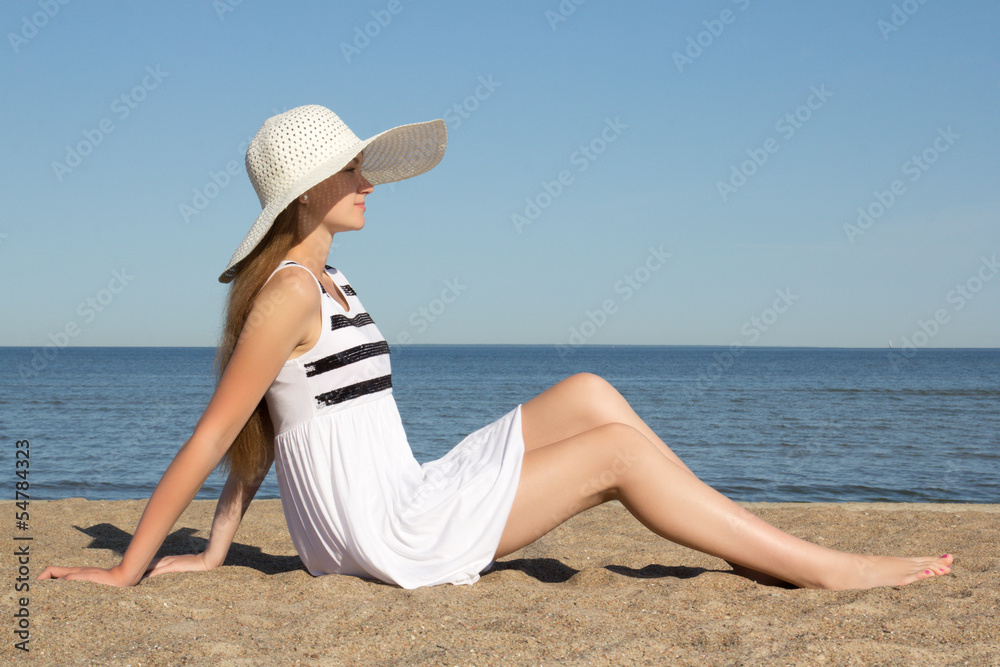 pretty woman in striped dress and hat sitting on the beach