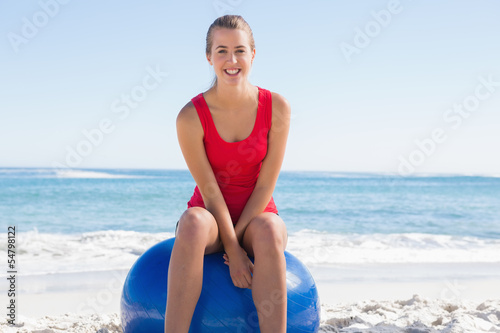 Fit young woman sitting on exercise ball smiling at camera