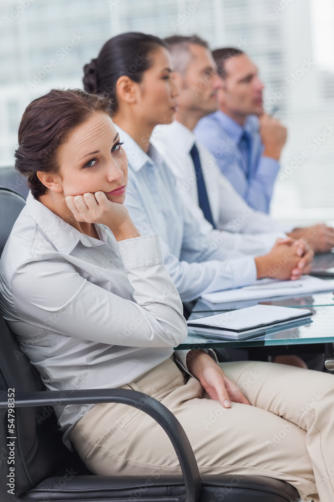 Bored businesswoman looking at camera while attending presentati Bored businesswoman looking at camera while attending presentati