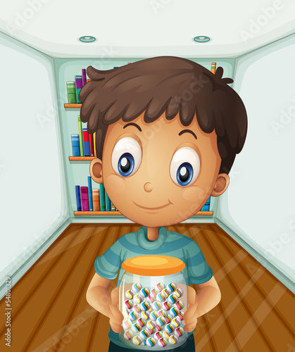 A boy holding a jar of candies in front of the bookshelves
