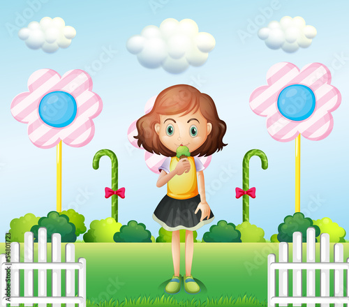 A girl eating an icecream near the fence with giant candies