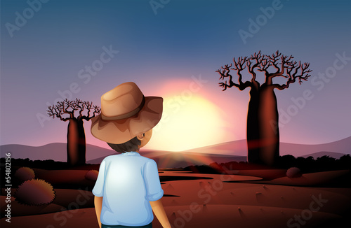 A boy with a hat watching the sunset in the desert