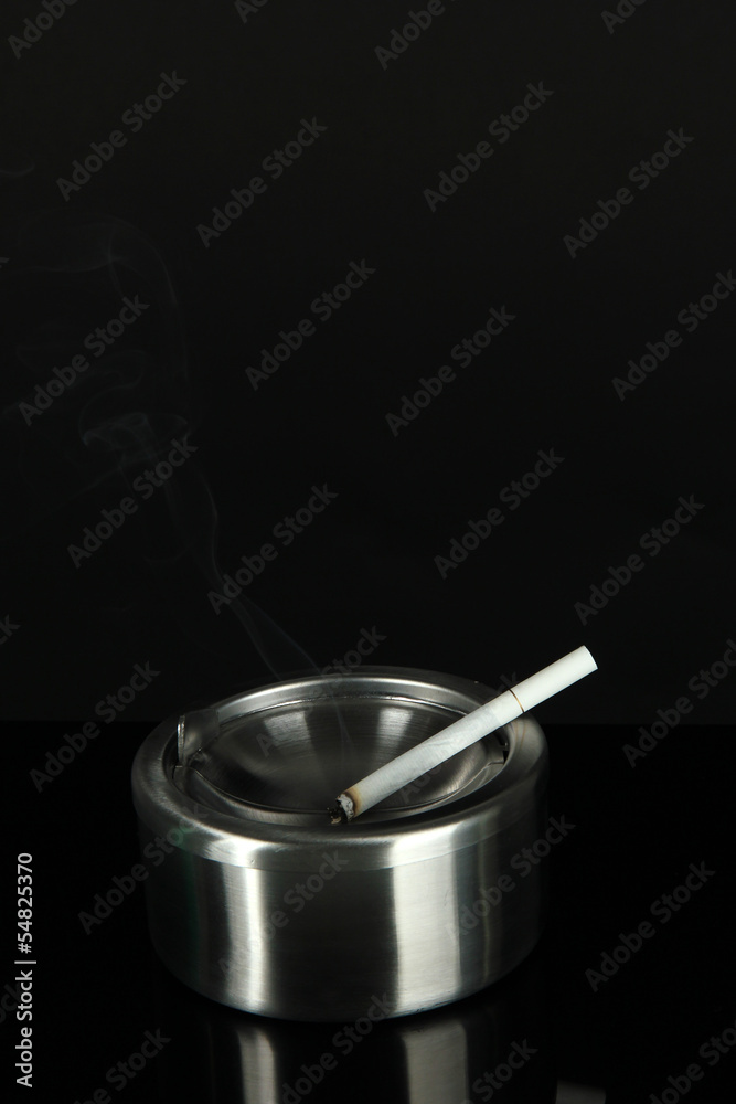 Metal ashtray and cigarette on black background Metal ashtray and cigarette on black background