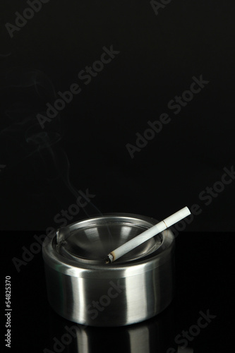 Metal ashtray and cigarette on black background