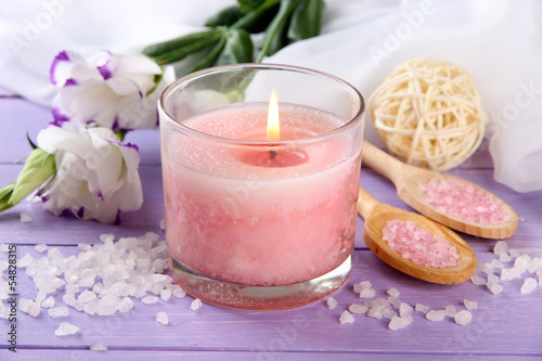 Beautiful pink candle with flowers on purple wooden background